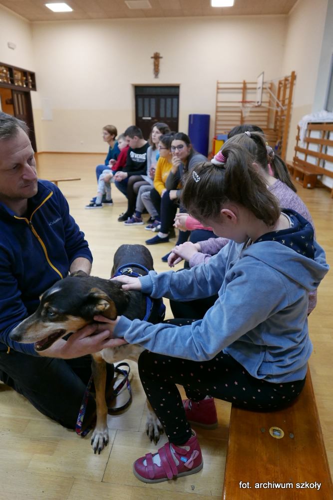 Instruktor trzyma psa, uczennica głaszcze go po grzbiecie.