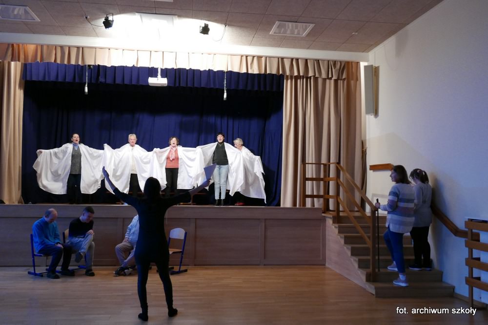 Uczniowie w białych strojach stoją na scenie.
