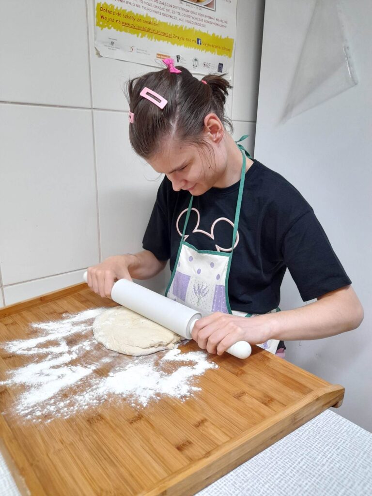 Uczennica na stolnicy wałkuje ciasto.