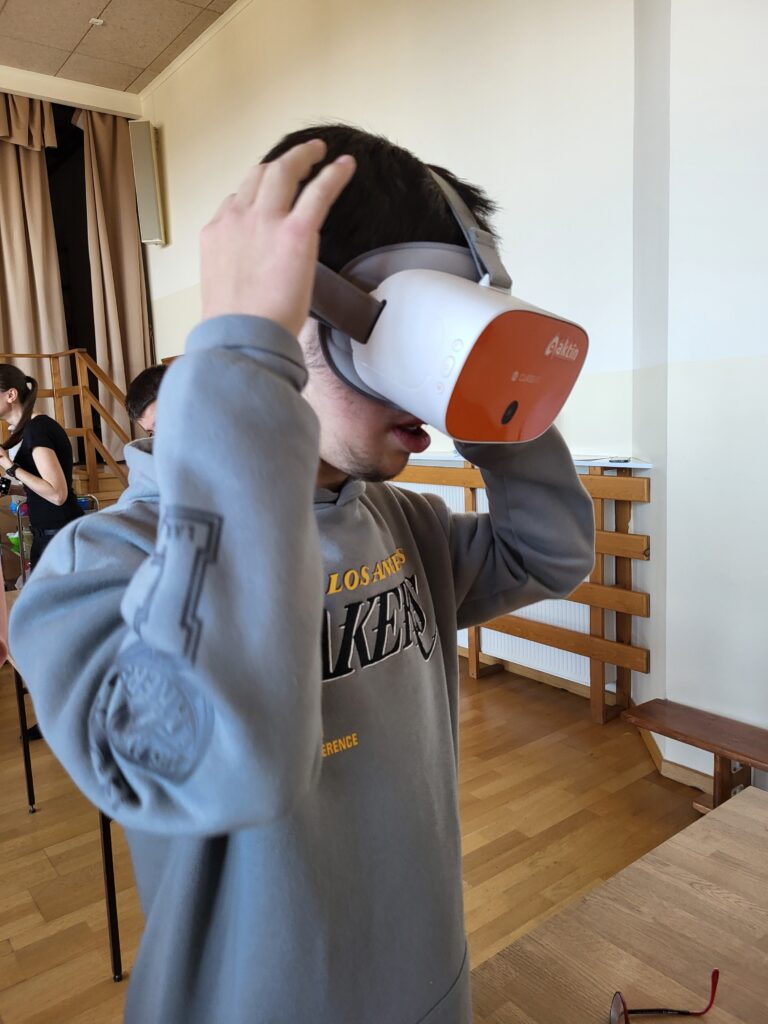 Osoba w szarej bluzie zakłada gogle VR, trzymając je obiema rękami.