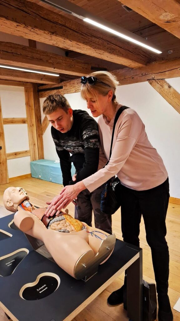 Kobieta prowadzi rękę młodego mężczyzny pokazując mu na manekinie do nauki anatomii położenie narządów w jamie brzusznej człowieka.