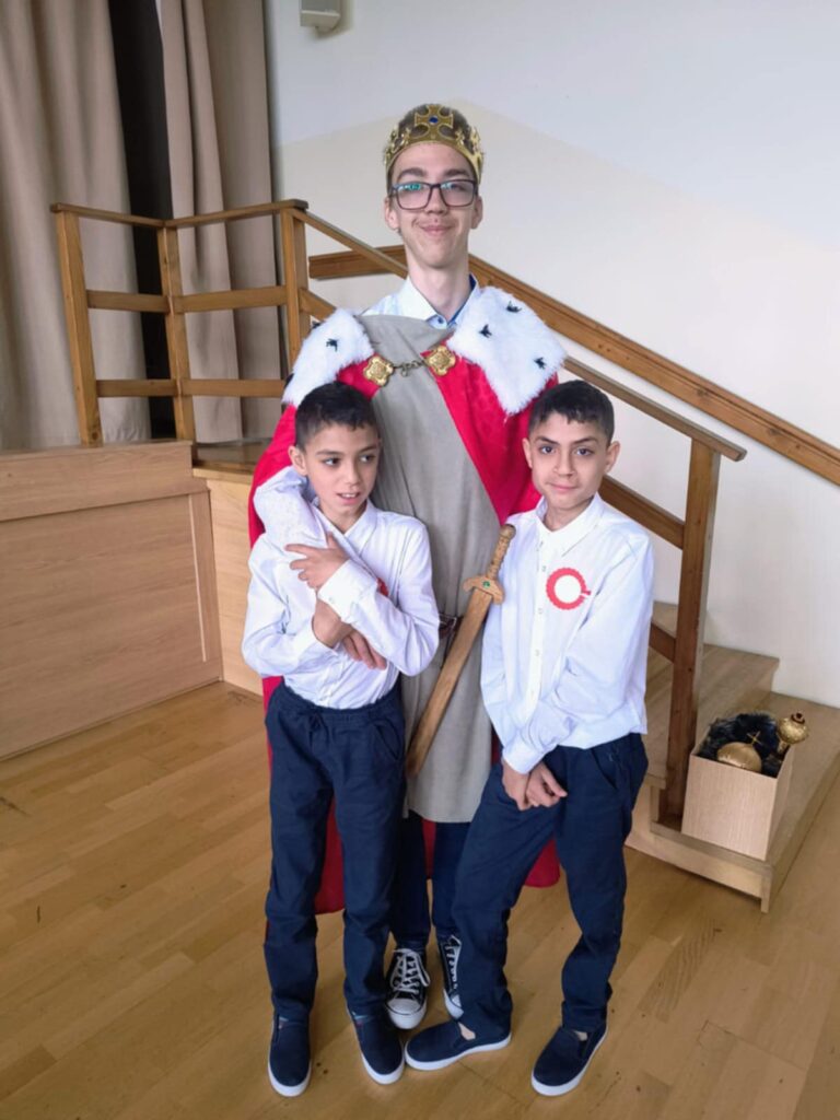 Młody mężczyzna w stroju króla stoi z dwojgiem małych chłopców. 