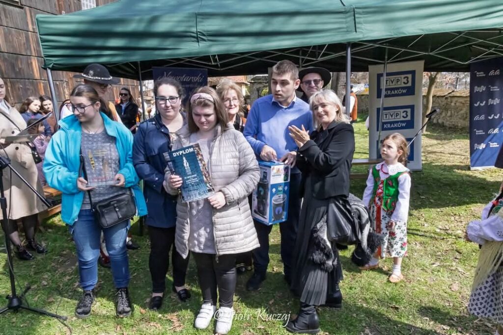 Grupa osób z nagrodami pozuje do zdjęcia na plenerowym wydarzeniu.