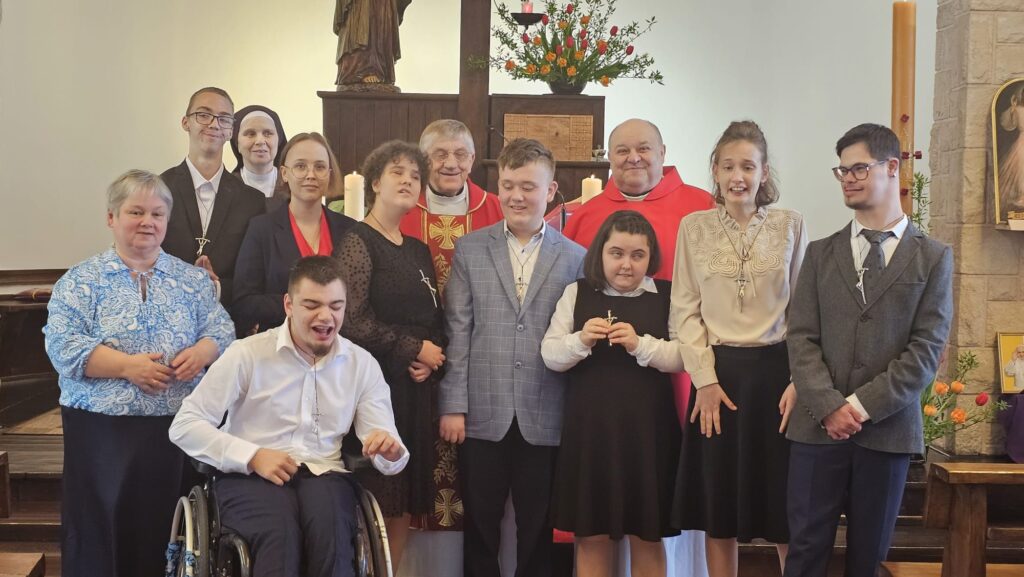 Grupowe zdjęcie w kościele przedstawiające uczestników ceremonii bierzmowania zgromadzonych wokół ołtarza.
