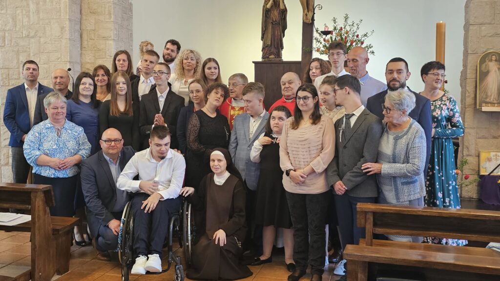 Grupowe zdjęcie w kościele przedstawiające uczestników ceremonii bierzmowania – młodzież, osoby duchowne i bliscy, zgromadzeni wokół ołtarza.