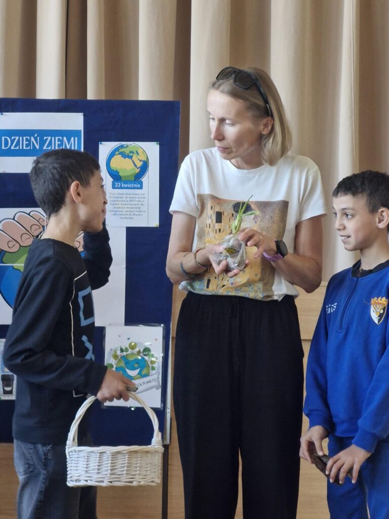 Nauczycielka rozmawia z dwoma chłopcami podczas szkolnych obchodów Dnia Ziemi, jeden z nich trzyma biały koszyk.