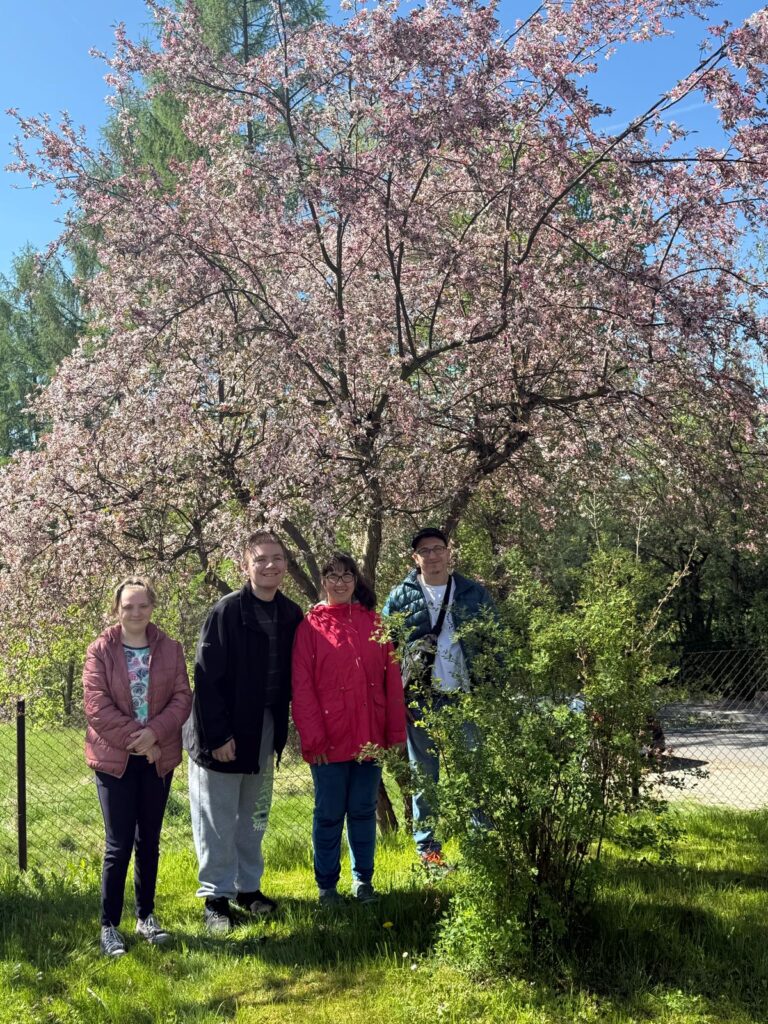 Grupa młodzieży stoi na tle kwitnącego drzewa w słoneczny dzień.