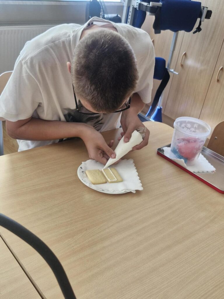 Chłopiec w okularach dekoruje ciastko białym lukrem.