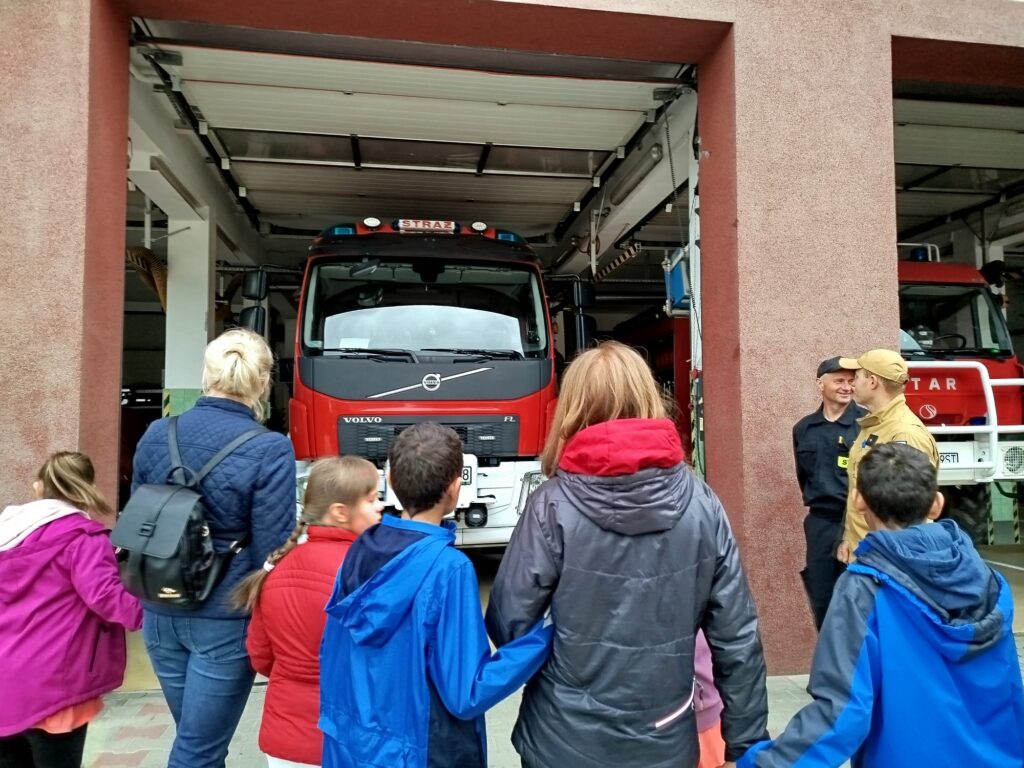 Dzieci wraz z nauczycielkami stoją przed otwartym garażem z pojazdami strażackimi.