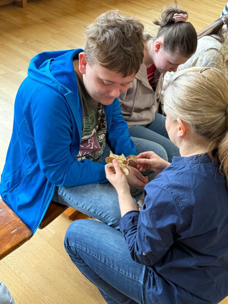 Nauczycielka kuca przy siedzącym uczniu pokazując mu model owada.