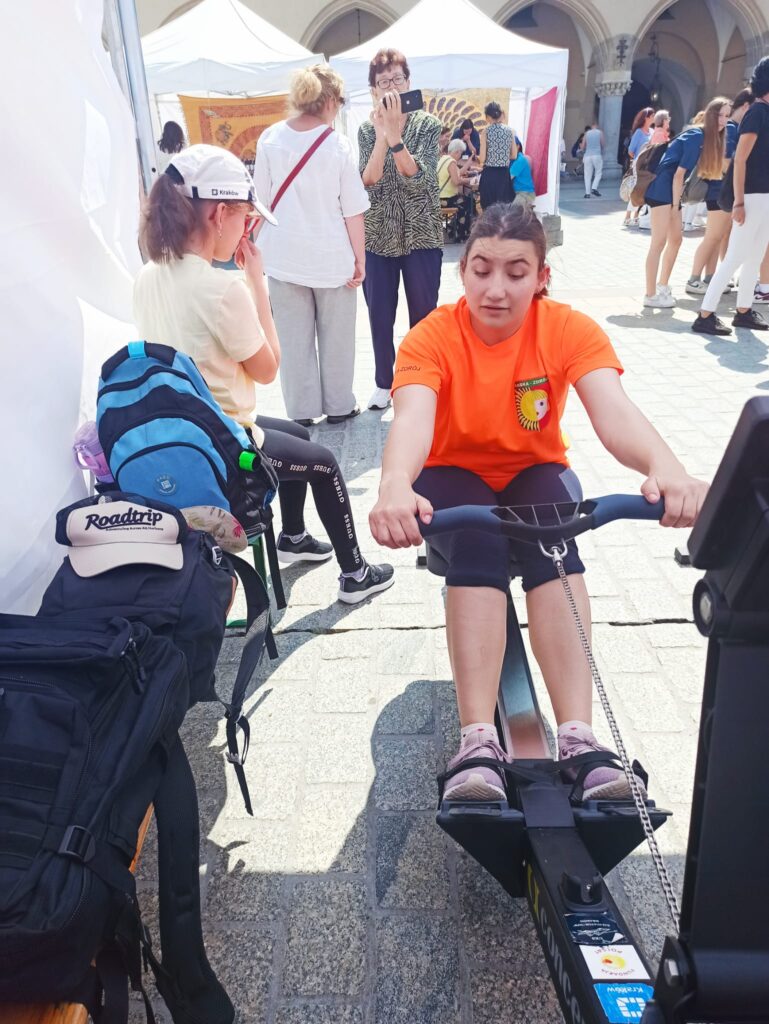 Młoda kobieta na ergometrze  w trakcie zawodów, w tle pozostali uczestnicy.