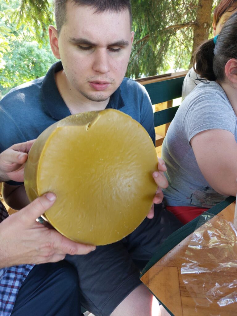 Młody mężczyzna trzyma w rękach dużą, okrągłą bryłę żółtego wosku pszczelego.