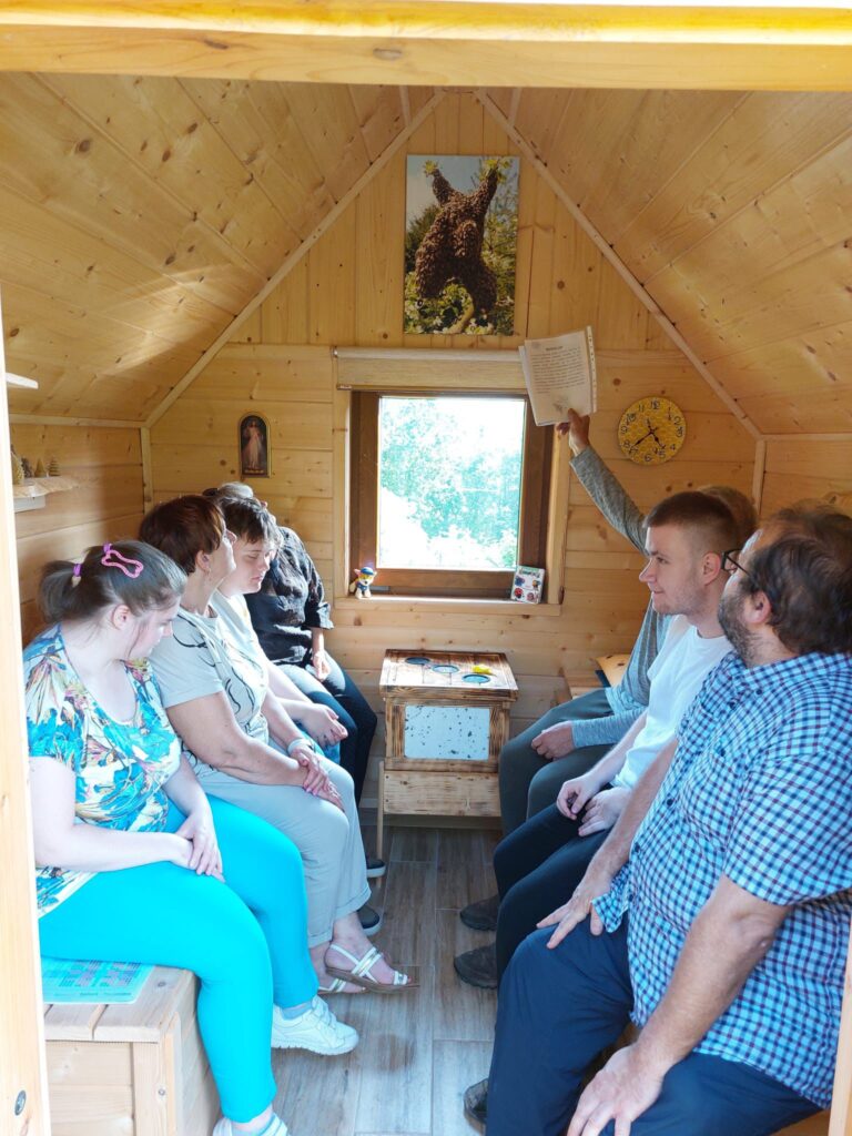 Grupa osób siedzi w drewnianym domku, który ogrzewają pszczoły.