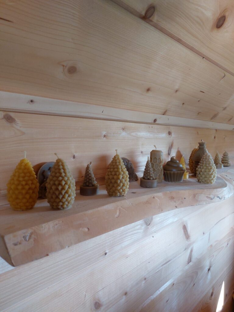 Woskowe świece o różnych kształtach stoją na drewnianej półce.