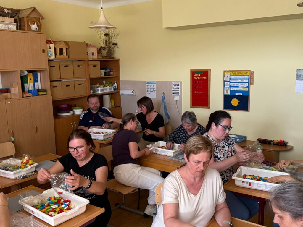 Uczestnicy szkolenia budują z klocków lego siedząc przy stolikach.