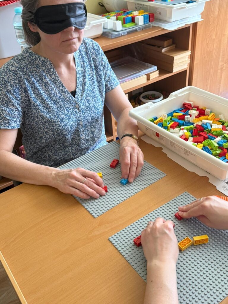 Kobieta z zasłoniętymi oczami układa brajlowskie klocki lego.