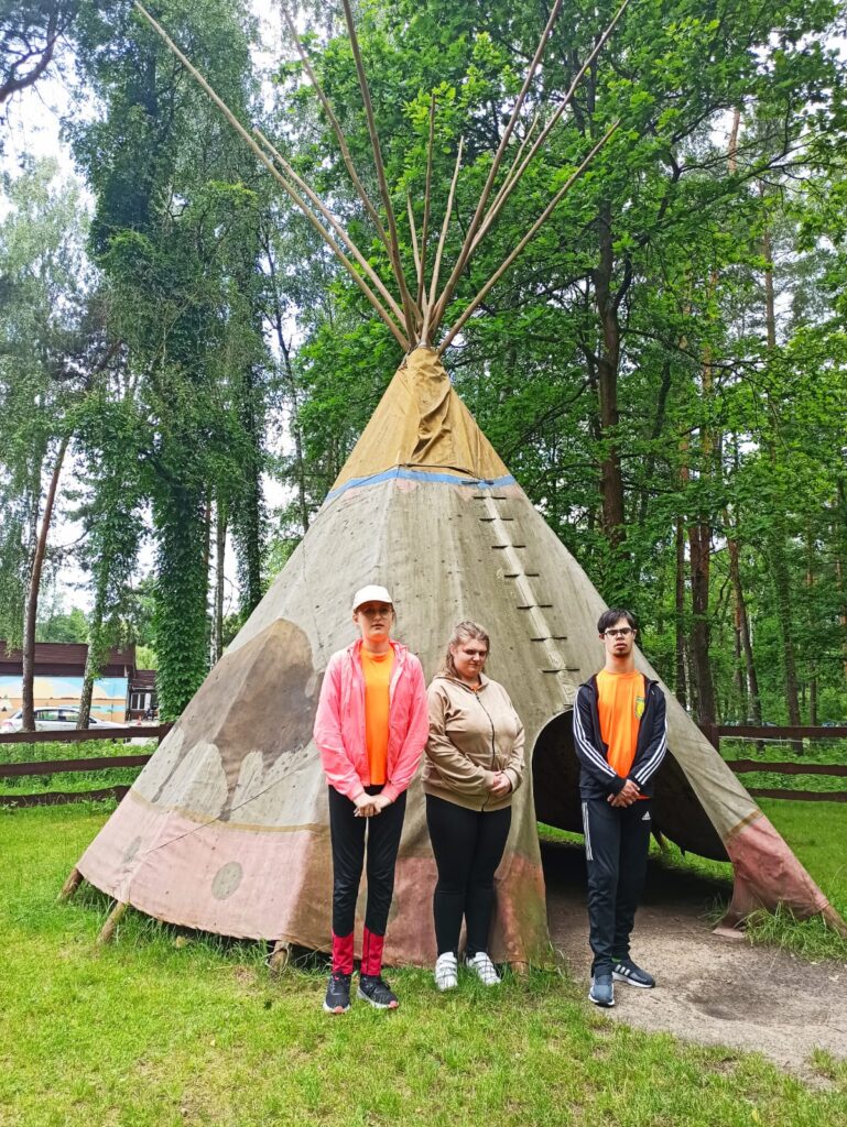 Dwie dziewczyny i chłopiec stoją przed namiotem indiańskim.