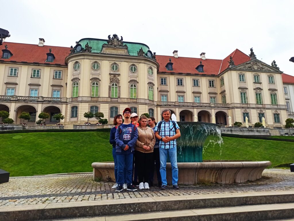 Sześć osób pozuje przed fontanną, w tle duży budynek.