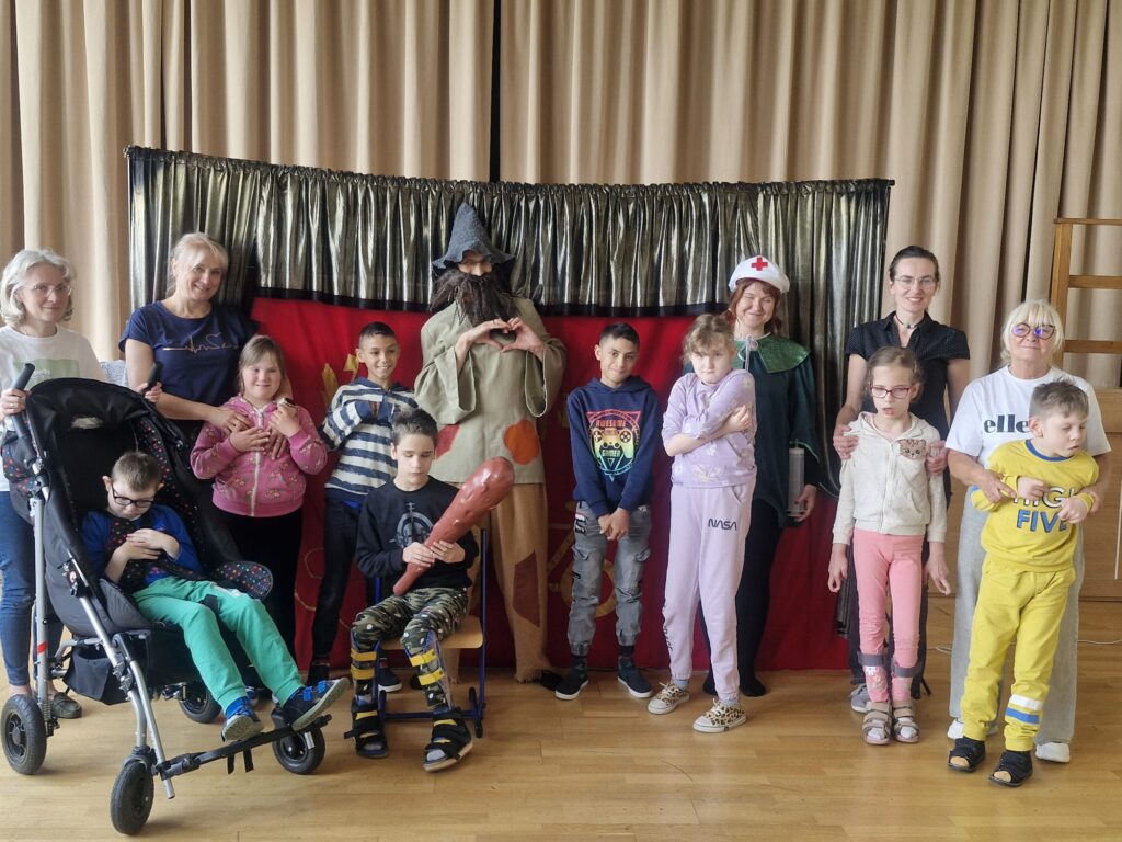 Grupowe zdjęcie dzieci i dorosłych z aktorami teatralnymi. 