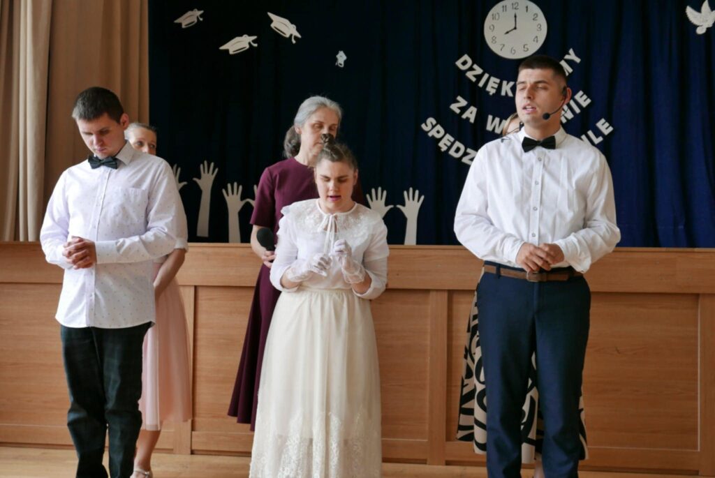 Dwóch młodych mężczyzn i kobieta ubranych elegancko, występują na scenie na tle dekoracji z napisem „Dziękujemy za wspólnie spędzone chwile”.