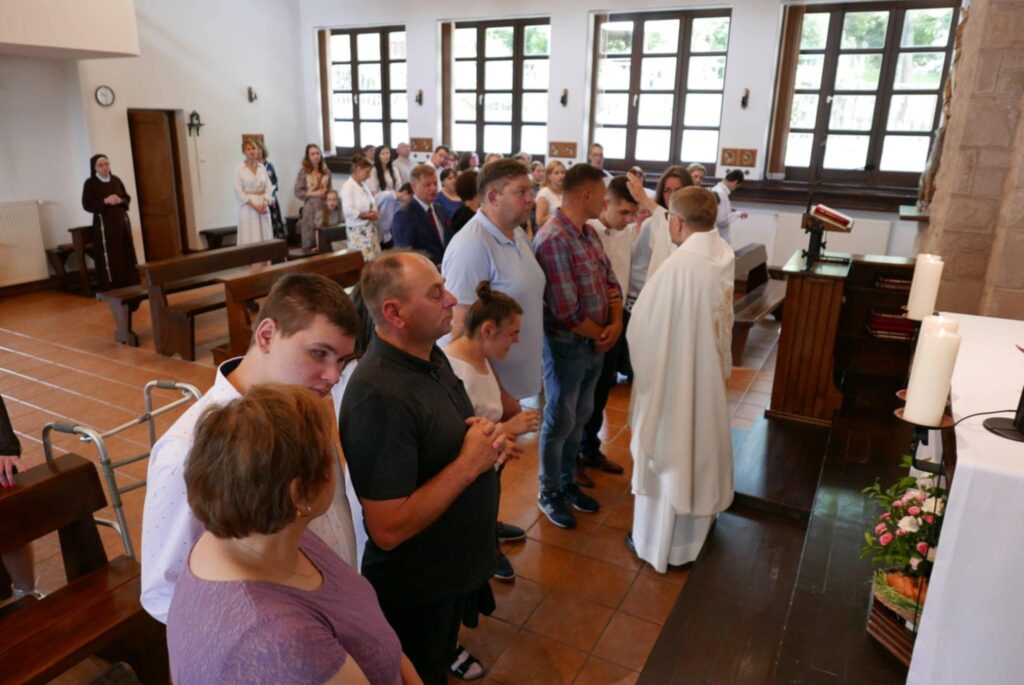Ludzie ustawieni w kolejce przy ołtarzu w kościele, uczestniczący w nabożeństwie z udziałem księdza. Indywidualne błogosławieństwo dla absolwentów.