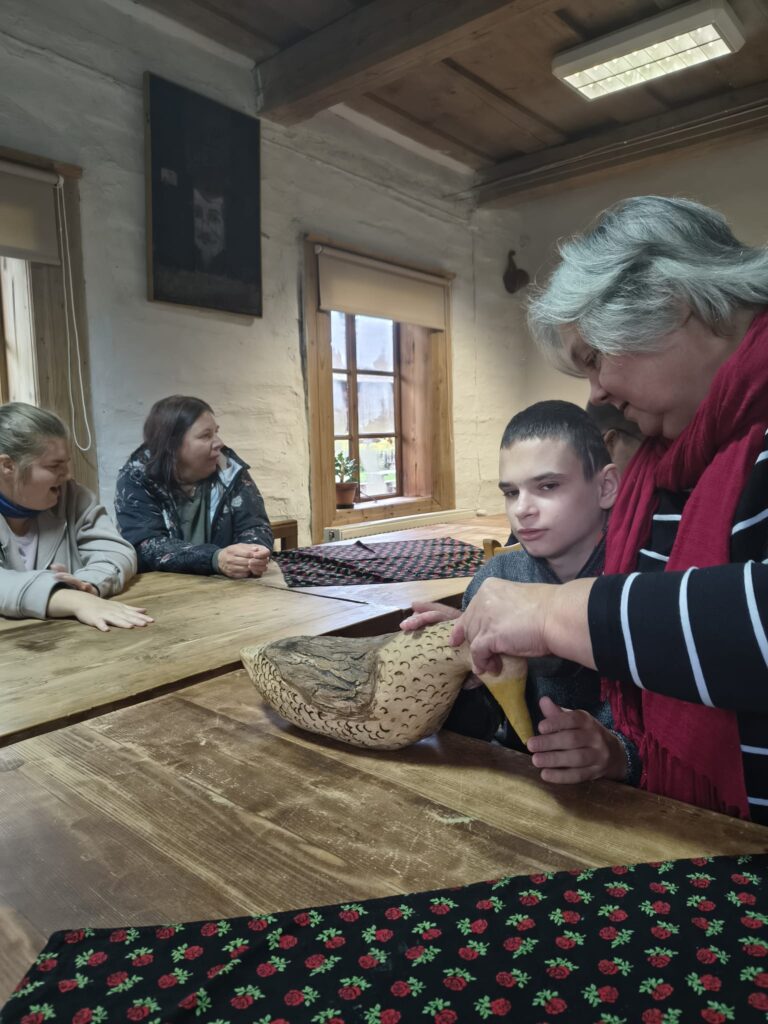 Chłopiec z pomocą nauczycielki dotyka drewnianej rzeźby ptaka.