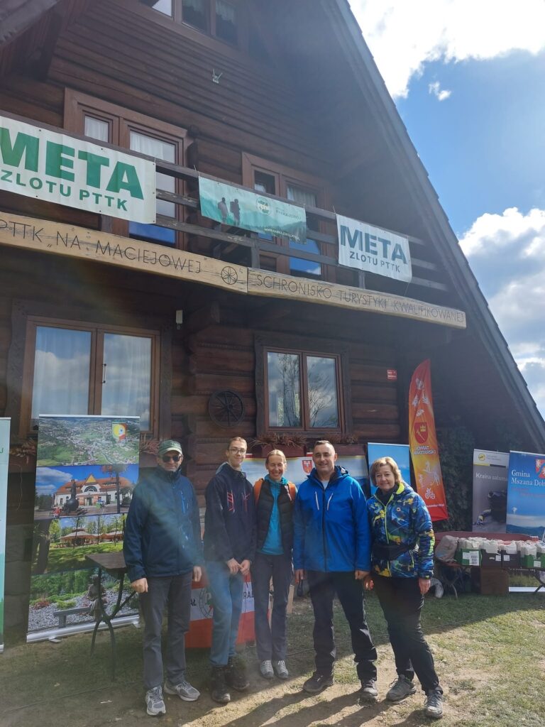 Grupa osób pozuje do zdjęcia przed drewnianym schroniskiem PTTK "Na Maciejowej".