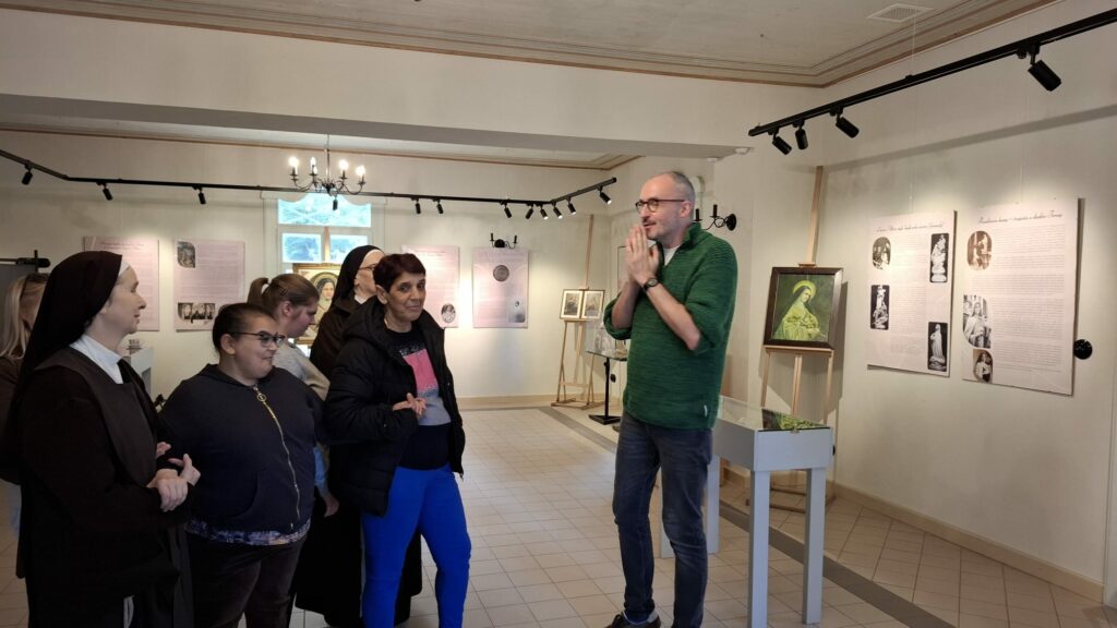 Grupa osób, w tym siostry zakonne, słucha przewodnika w muzeum poświęconym świętej Teresie z Lisieux.