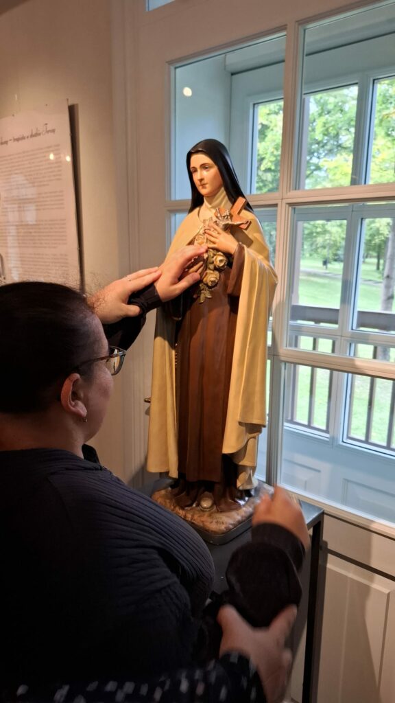 Kobieta dotyka figurę św. Teresy z Lisieux stojącą przy oknie.