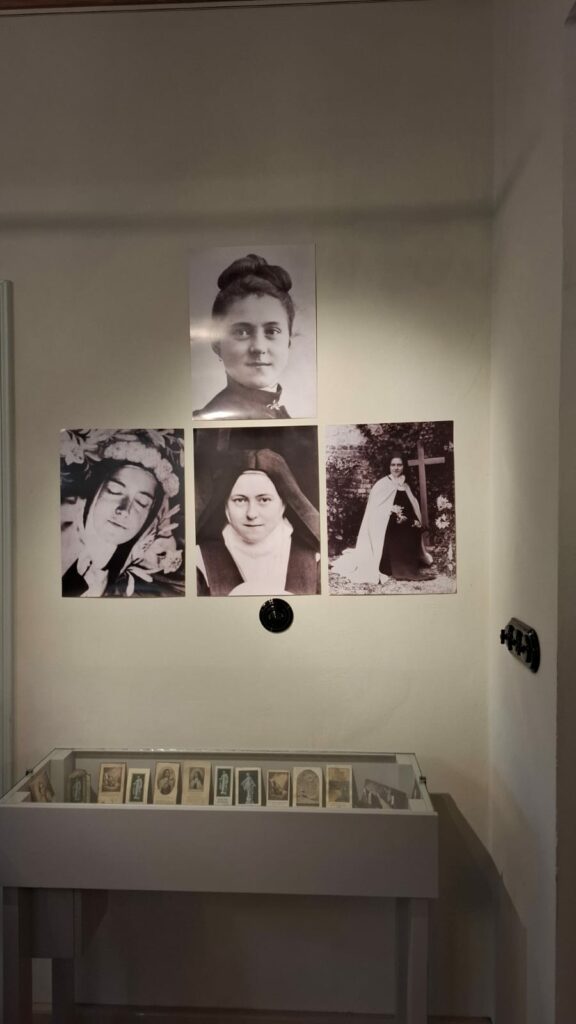 Ściana z czarno-białymi fotografiami św. Teresy z Lisieux i gablotą z dewocjonaliami.