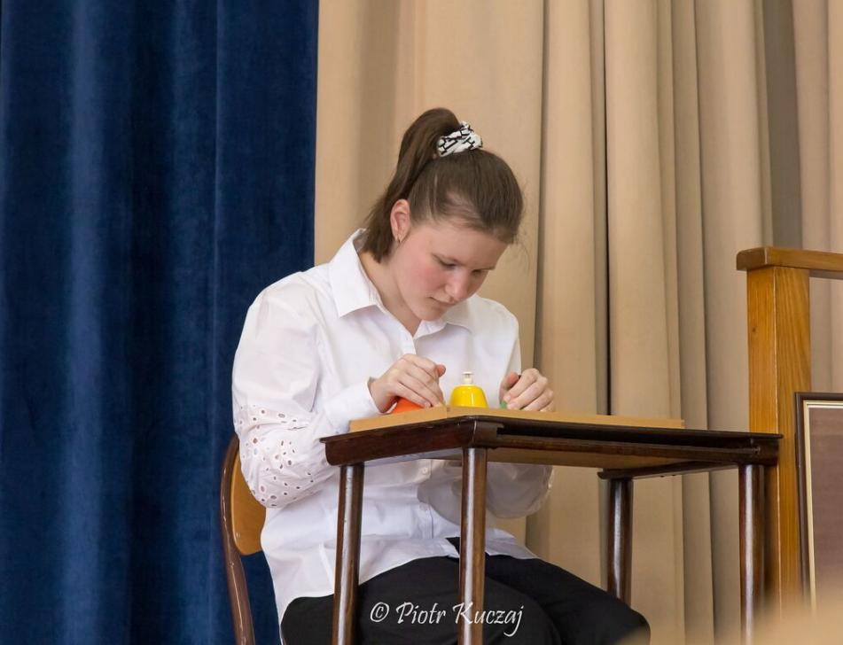 Młoda kobieta w białej bluzce siedzi przy stoliku i gra na dzwonkach naciskowych.