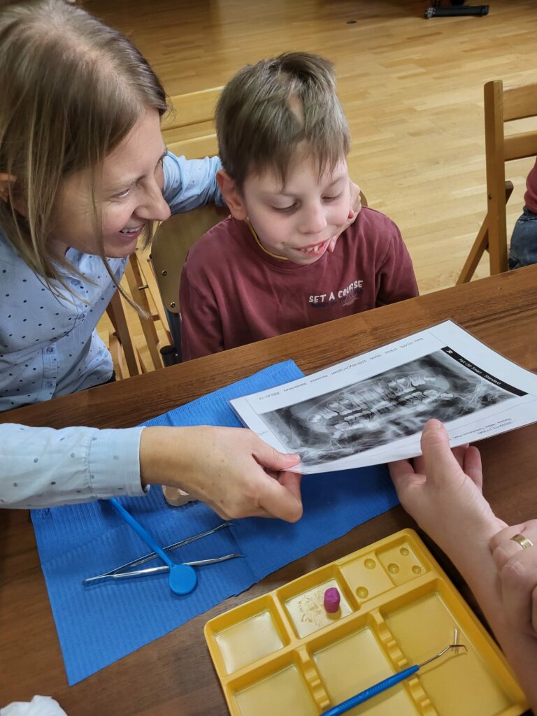Chłopiec z pomocą nauczyciela ogląda zdjęcie rentgenowskie zębów.
