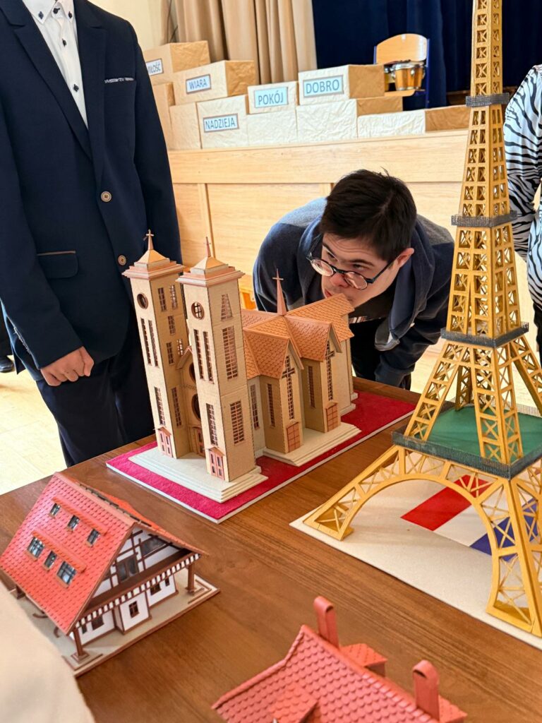 Chłopiec ogląda z bliska makietę katedry, obok znajdują się modele wieży Eiffla i innych budynków.