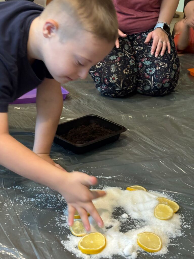 Chłopiec klęczy na podłodze i dotyka ręką soli z plasterkami cytryny leżącej przed nim.