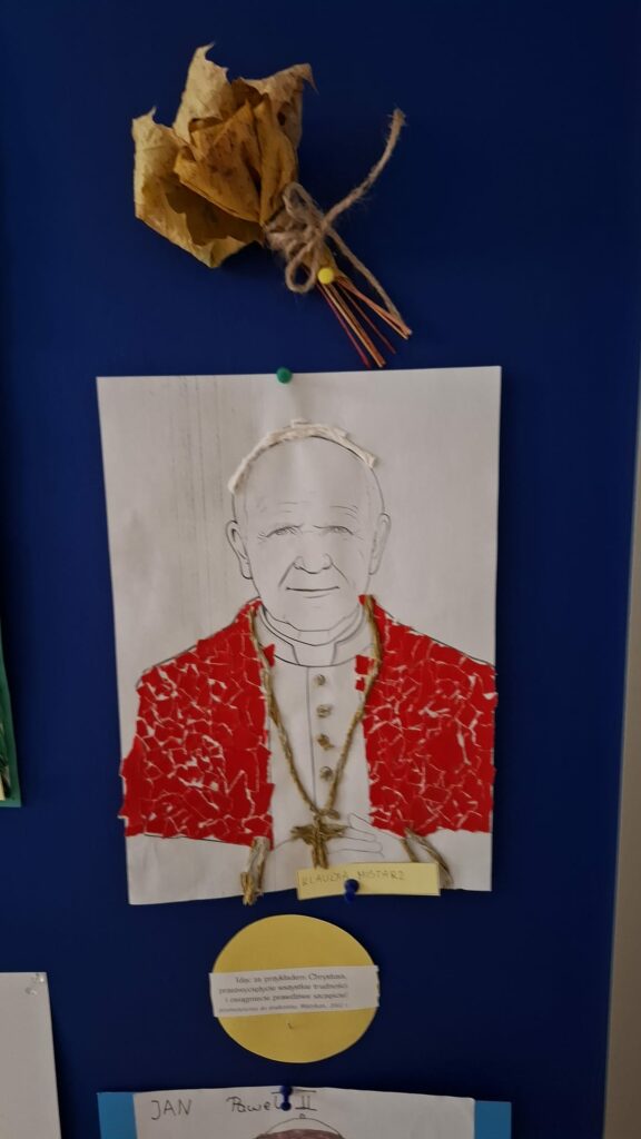 Zbliżenie na pracę plastyczną o Janie Pawle II w czerwonym ornacie, z papieru i sznurka.