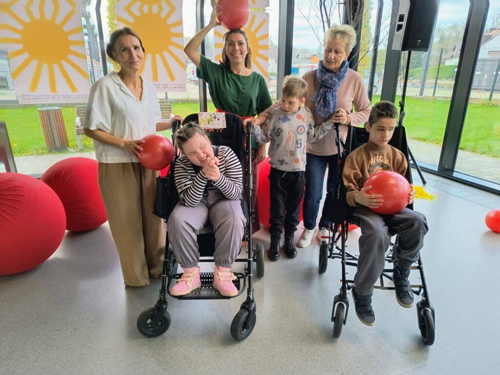 Trzy kobiety i troje dzieci. Dziewczynka i chłopiec siedzą w dużych wózkach. dwie kobiety i chłopiec w wózku trzymają czerwone piłki.