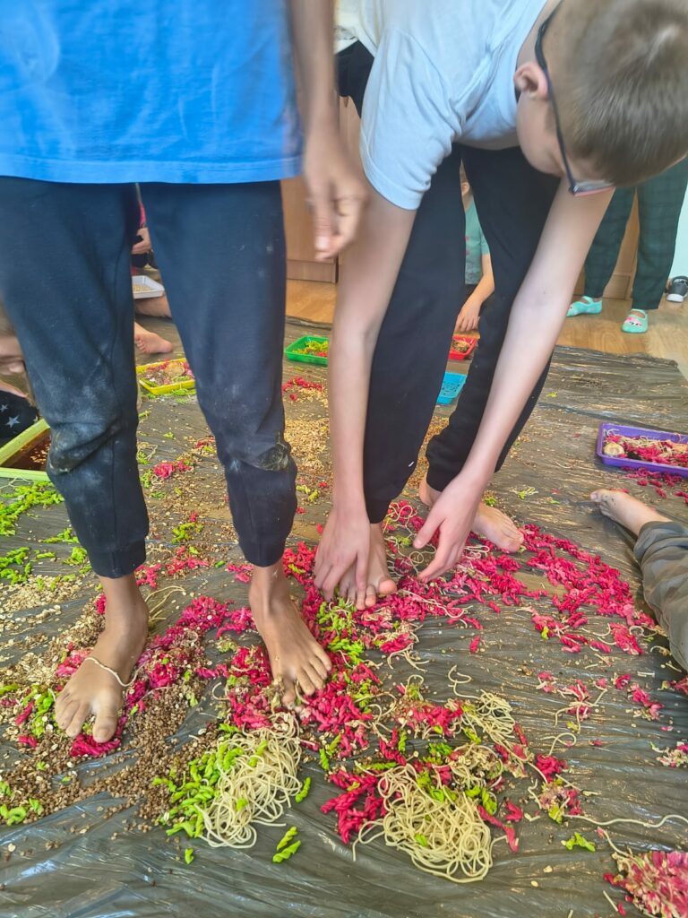 Chłopcy spacerują gołymi stopami po różnych kolorowych materiałach sypkich.