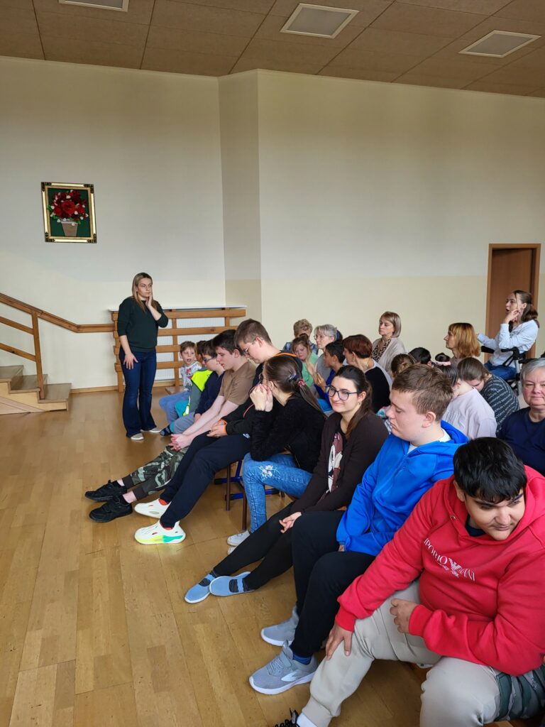 Grupa osób siedzi na sali i uważnie słucha prowadzącego.