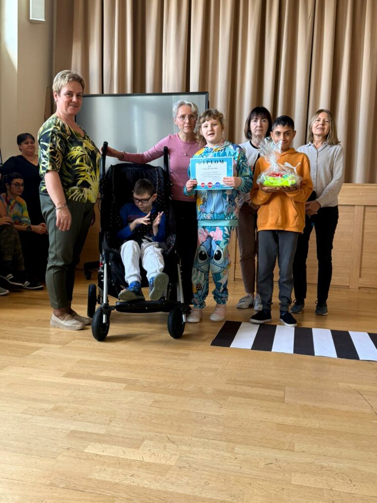 Grupa osób pozuje do zdjęcia dziewczynka trzyma w rękach dyplom, a chłopiec nagrodę.