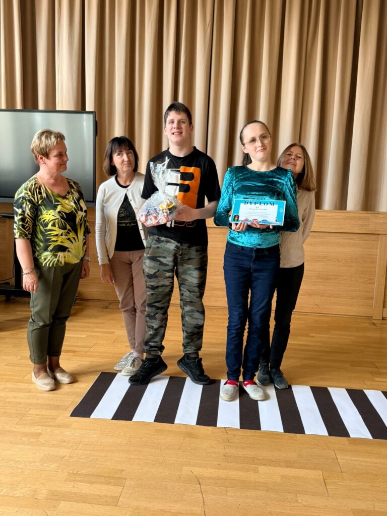 Chłopiec i dziewczyna oraz trzy dorosłe kobiety. Chłopiec trzyma nagrodę, a dziewczynka prezentuje dyplom.