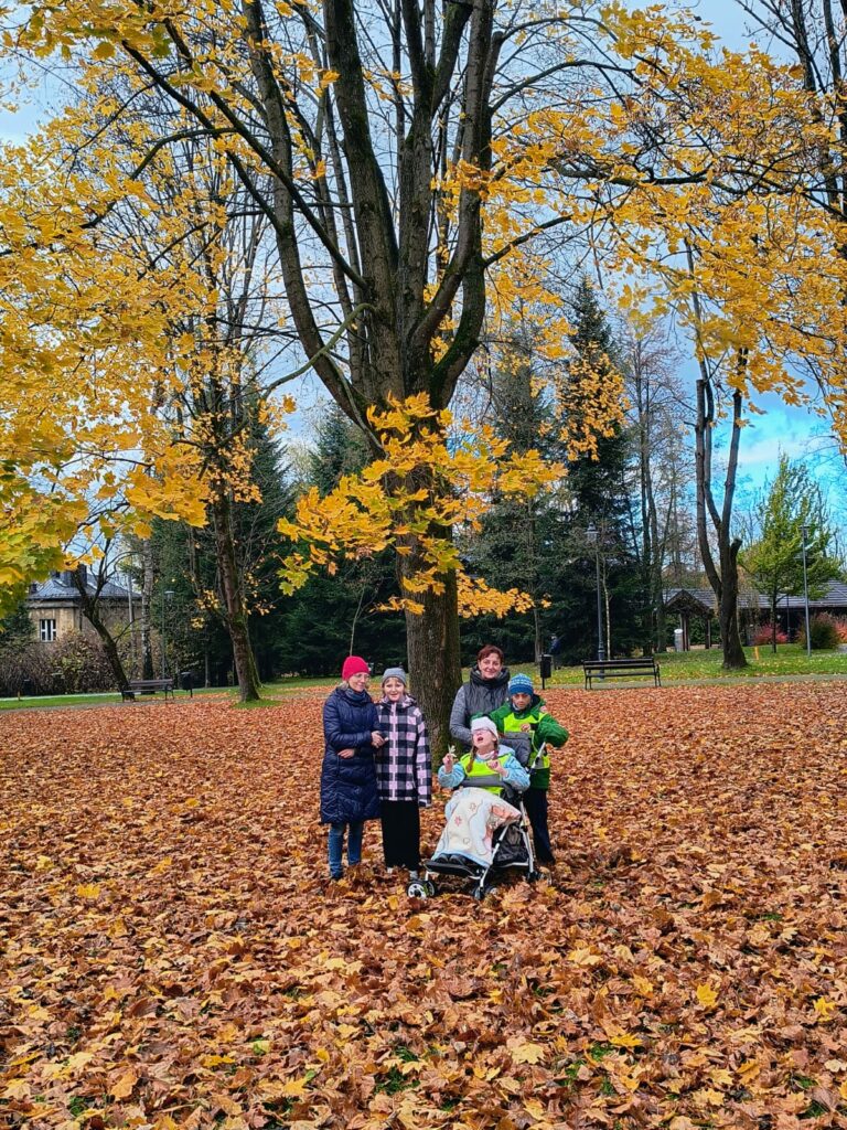Dwie kobiety i trójka dzieci pozują do zdjęcia w jesiennym parku mając pod stopami dywan z opadłych liści.