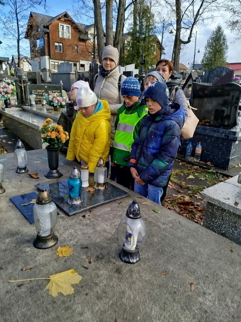 Dwie kobiety z grupą dzieci stoją przy grobie na cmentarzu pogrążeni w zadumie.