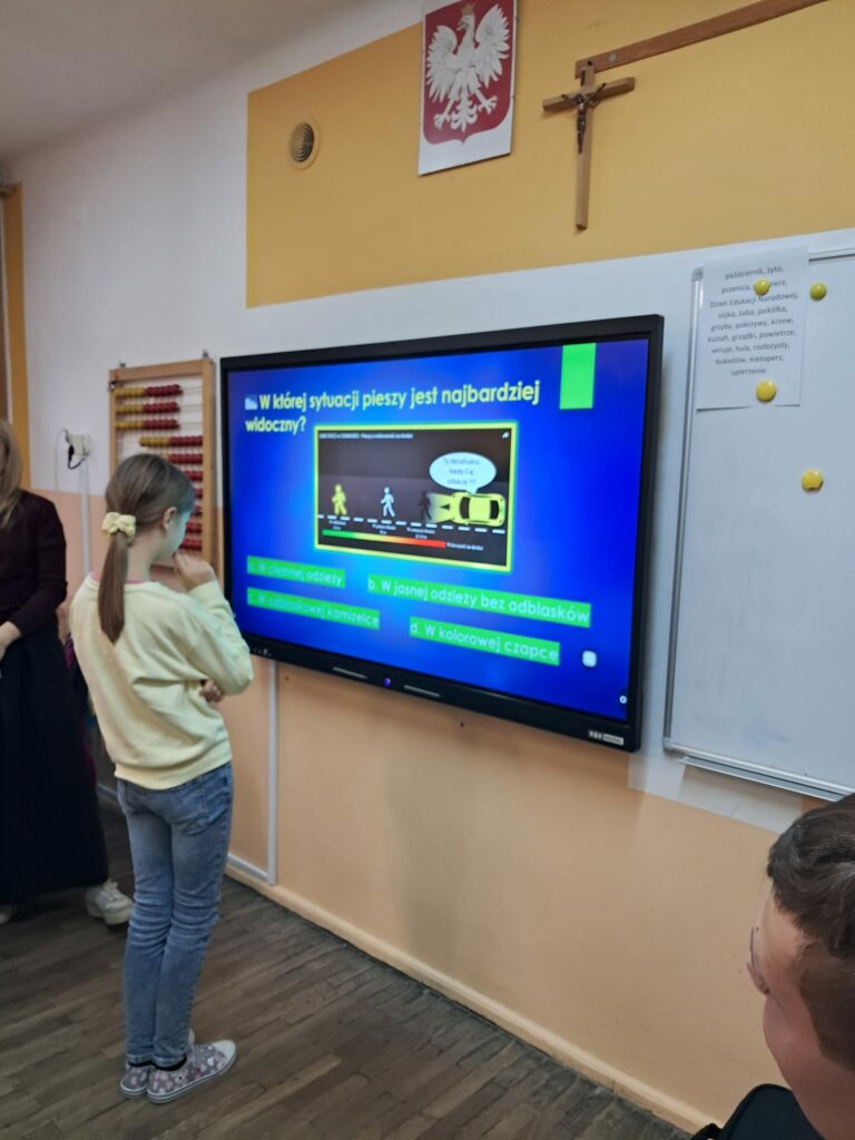 Dziewczynka rozwiązuje quiz wyświetlany na dużym ekranie multimedialnym.