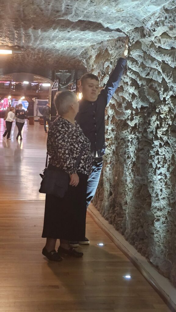 Kobieta i młody mężczyzna spacerują podziemnym korytarzem, a chłopak dotyka oświetlonej ściany z soli.