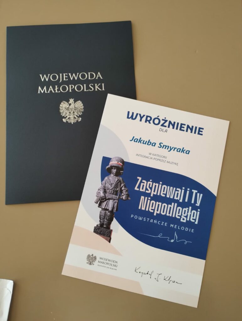 Dyplom wyróżnienia leży obok granatowej teczki z napisem Wojewoda Małopolski.