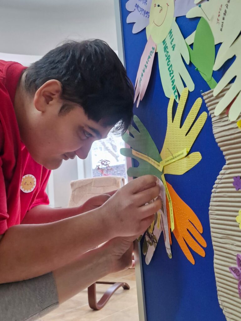 Młody mężczyzna w czerwonej bluzie przypina kartki do tablicy.