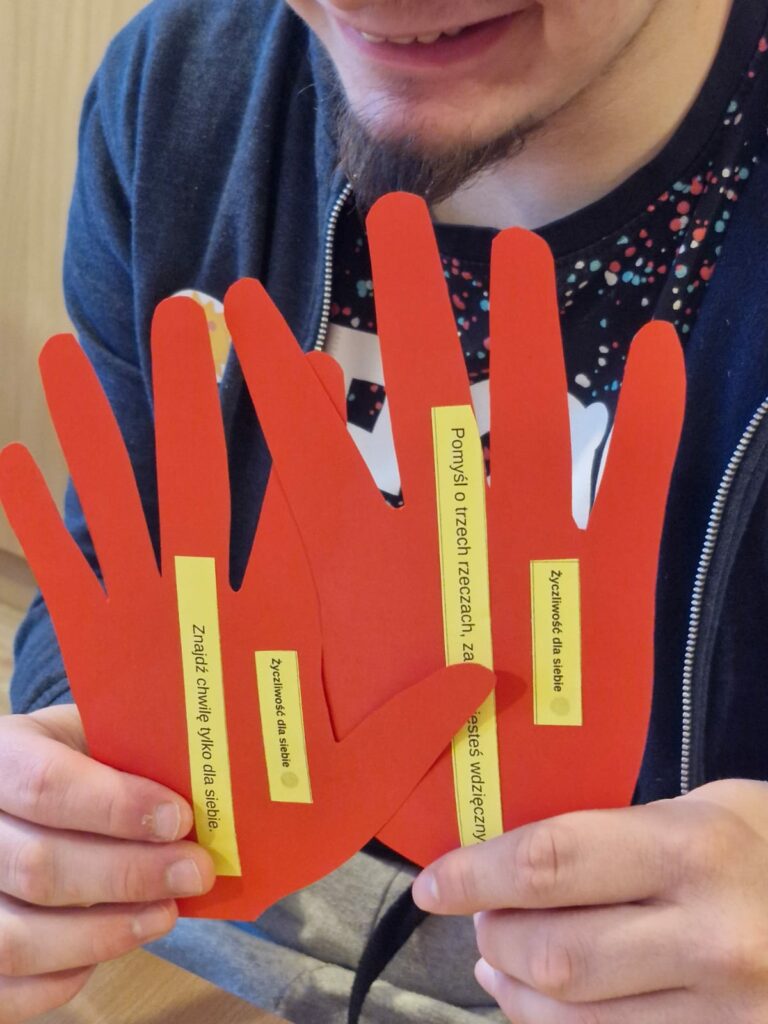 Uśmiechnięty młody mężczyzna trzyma w rękach wycięte czerwone dłonie z napisami.