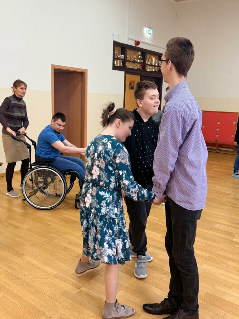 Dwóch chłopców i dziewczynka tańczą razem w kółeczku trzymając się za ręce.