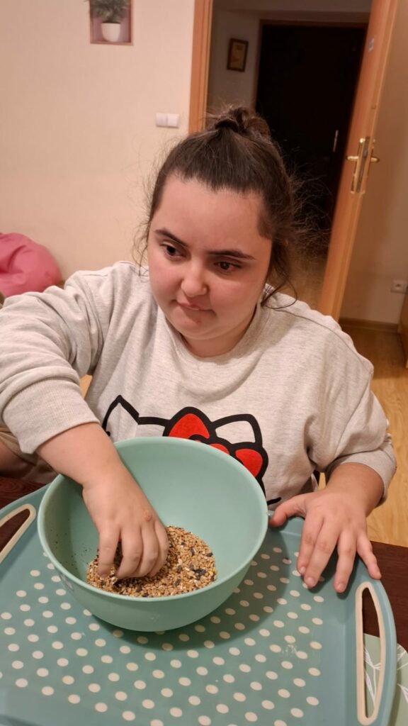 Dziewczynka w szarej bluzce miesza ziarna rękom w misce