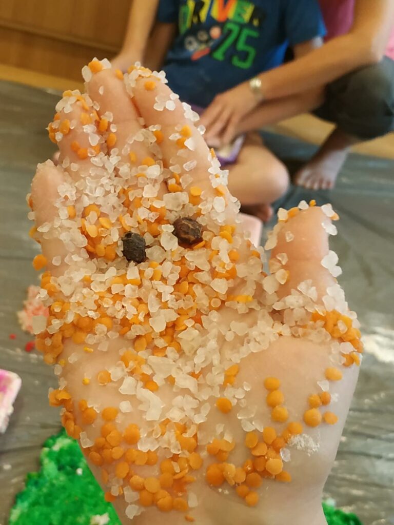 Dłoń dziecka pokryta biało żółtym materiałem sypkim z oczkami ziela angielskiego